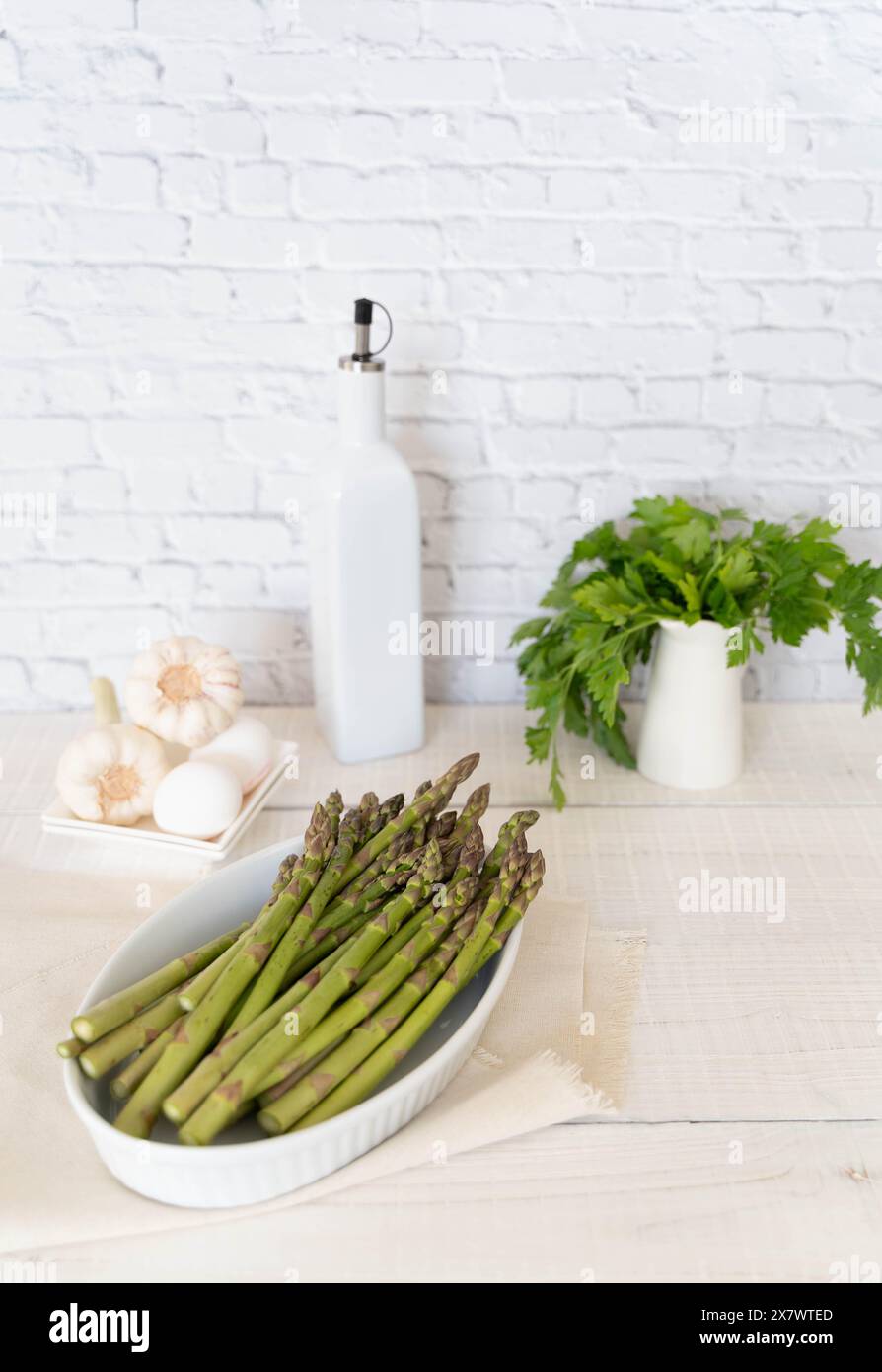 Crisp Green Asparagus shown in baking tray, ready for cooking. In the background the produce is framed by olive oil bottle and other ingredients Stock Photo