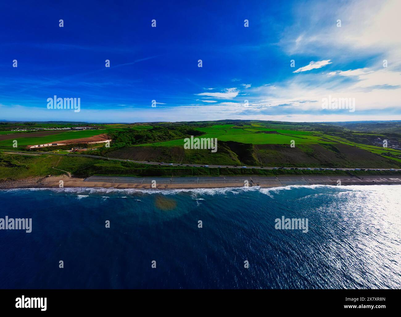 Aerial view of a coastal landscape with a beach, green fields, and a ...