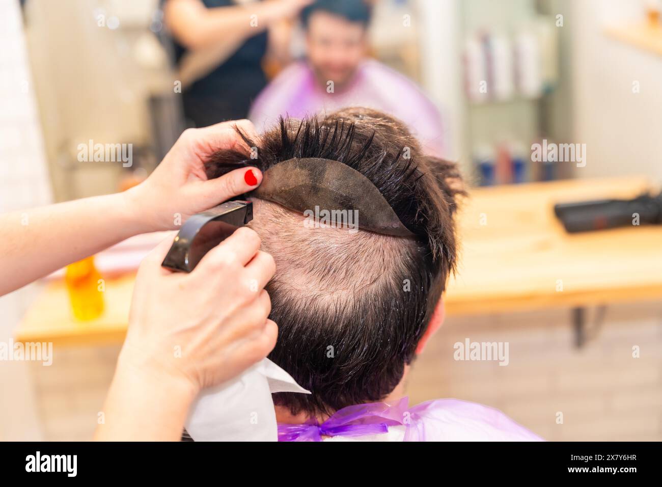 Rear view of the hands of a hairdresser wetting the head of a client to ...