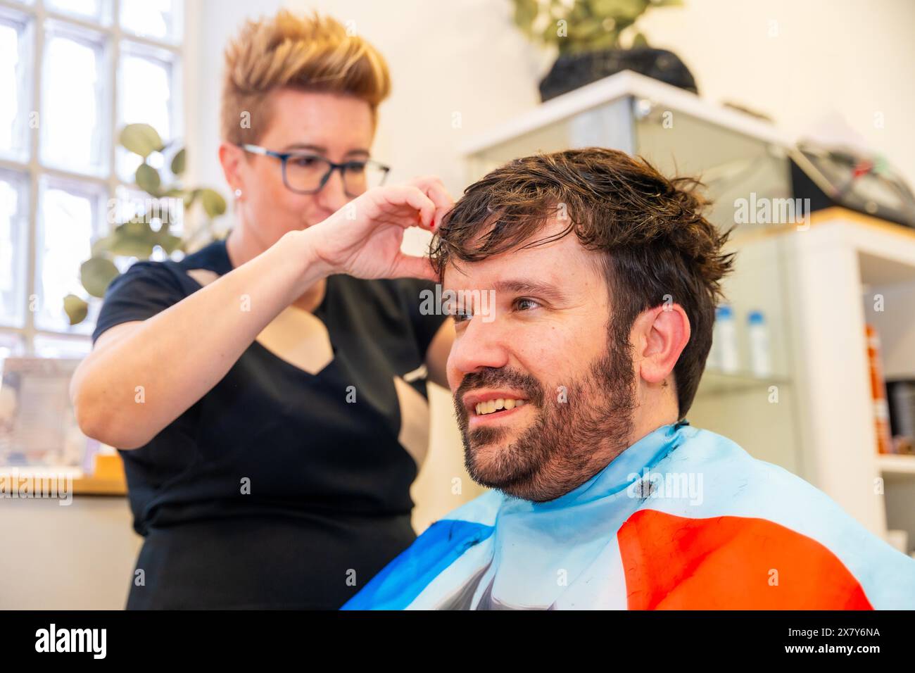 Hairdresser placing a capillary prosthesis to a bald man sitting in a ...