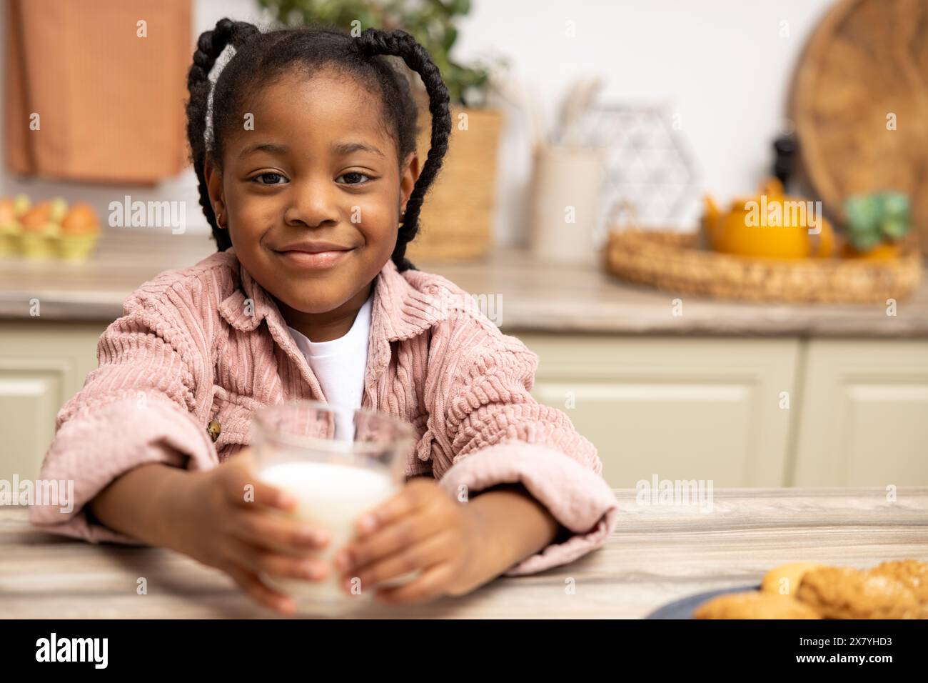 Happy African American kid drinking milk with cookies in kitchen Stock Photo