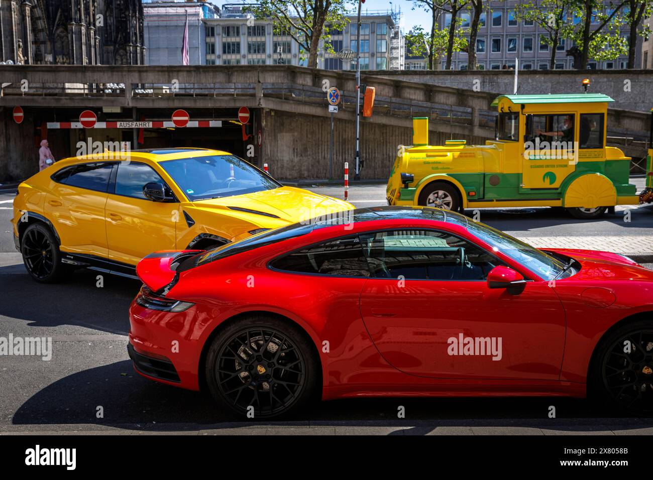 a Porsche 911 and a Lamborghini Urus stand in front of the of the Excelsior Hotel Ernst, in the background the Cologne Bimmelbahn for city tours, Colo Stock Photo