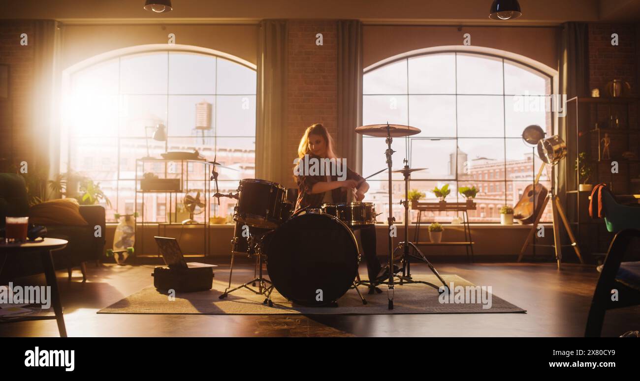Young Female Playing Drums During a Band Rehearsal in a Loft Studio with Warm Sunlight at Daytime. Drummer Girl Practising Before a Live Concert on Stage With Big Audience. Stock Photo