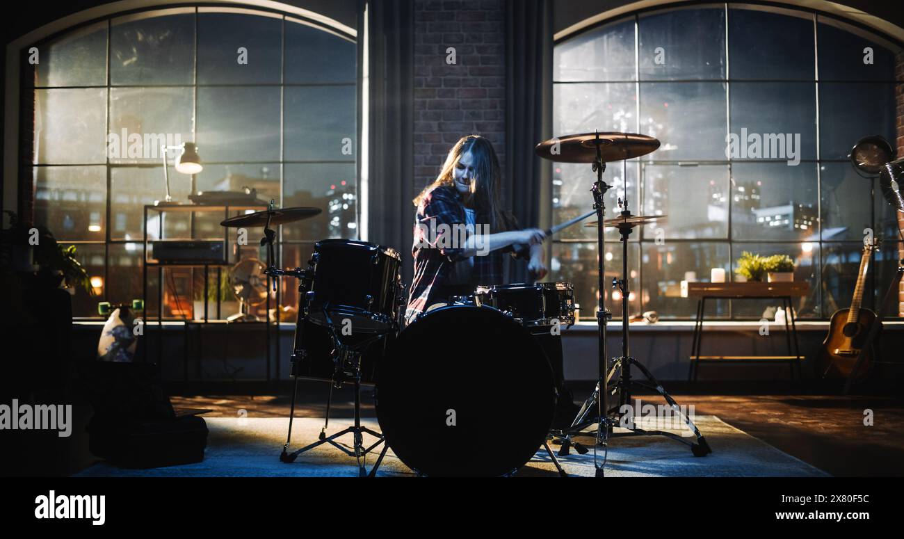 Young Female Playing Drums During a Band Rehearsal in a Loft Studio During an Evening or Night Session. Drummer Girl Practising Before a Live Concert on Big Stage with Audience. Stock Photo