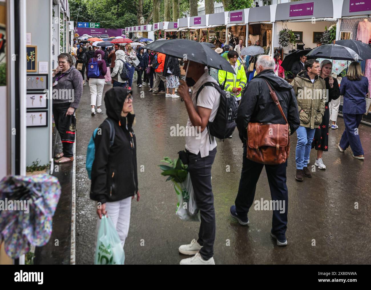 London, UK. 21st May, 2024. People with umbrellas stroll along Eastern Avenue with its exhibitors and shops. Following yesterday's press day with beautiful, warm sunshine throughout, today has been a lot of rain in the afternoon at Chelsea Flower Show, but visitors appear to have made the most it anyway. Credit: Imageplotter/Alamy Live News Stock Photo