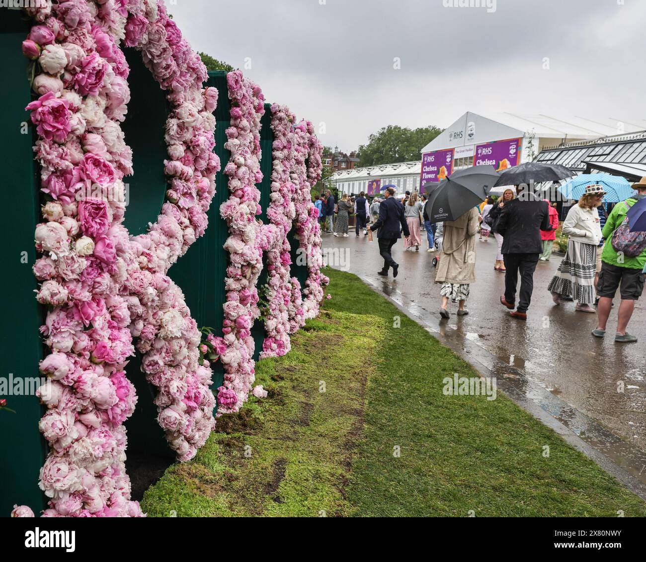 London, UK. 21st May, 2024. People with umbrellas stroll past the RHS sign. Following yesterday's press day with beautiful, warm sunshine throughout, today has been a lot of rain in the afternoon at Chelsea Flower Show, but visitors appear to have made the most it anyway. Credit: Imageplotter/Alamy Live News Stock Photo