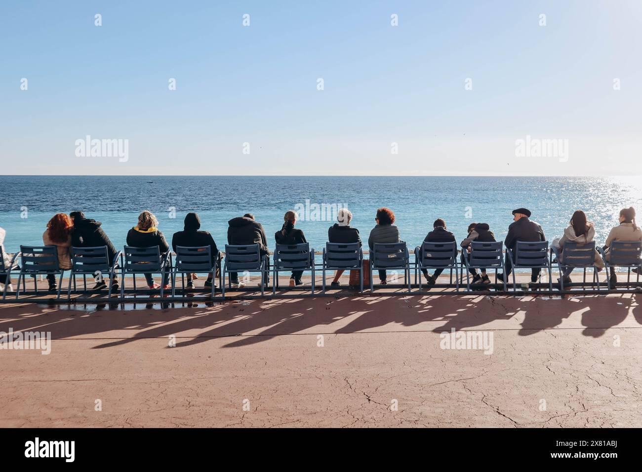 Nice, France - 15.01.2023 : People sitting on the famous blue chairs in Nice, in front of the sea on the Promenade des Anglais Stock Photo