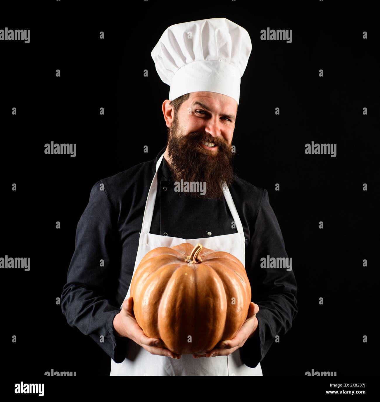 Smiling male chef in uniform with pumpkin. Bearded man in chef hat with squash. Organic food. Cook chef in white apron with pumpkin for culinary Stock Photo