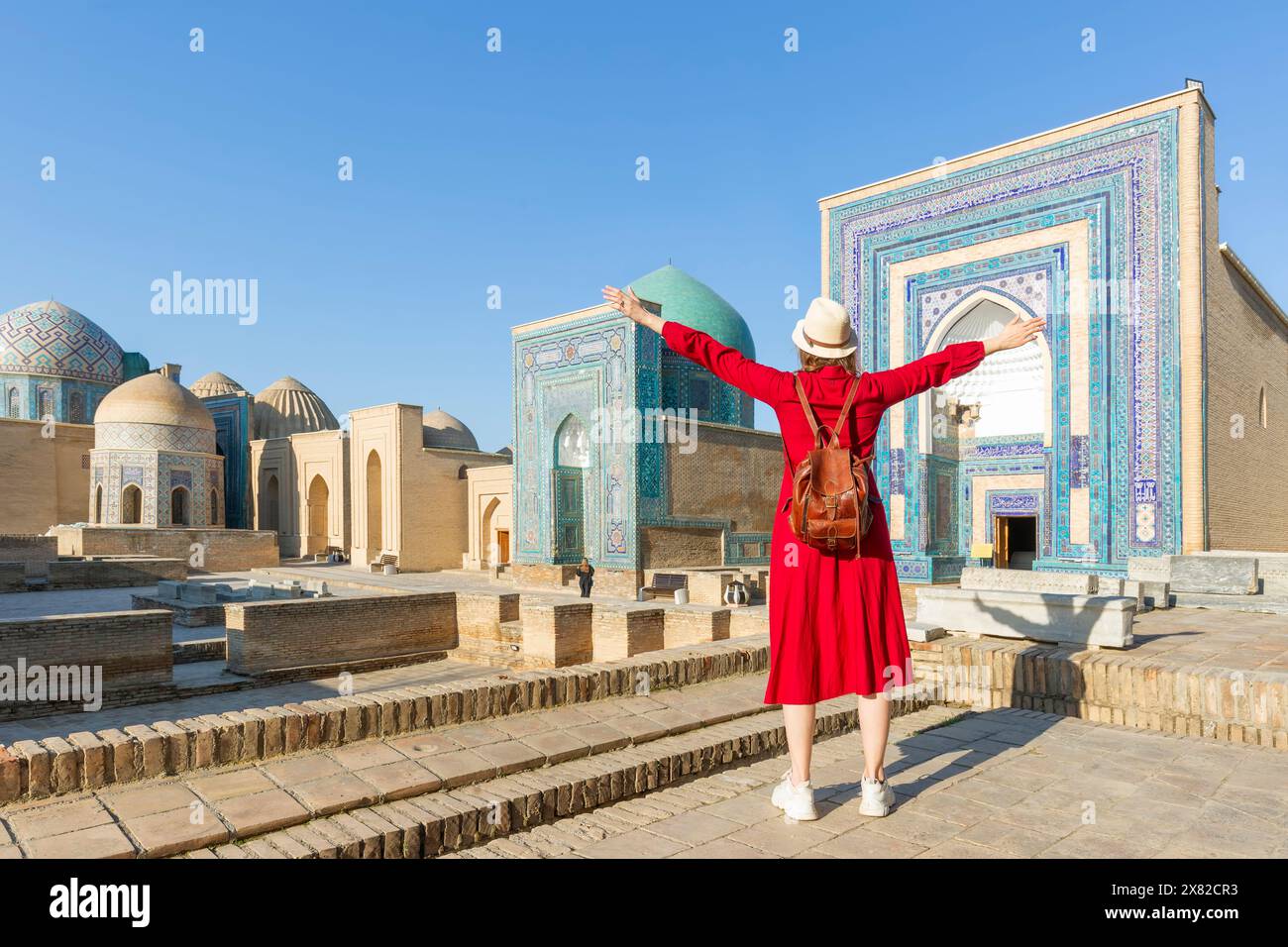 Young tourist dressed in red with arms raised in front of the Shah-I-Zinda memorial complex in Samarkand, Uzbekistan. Stock Photo