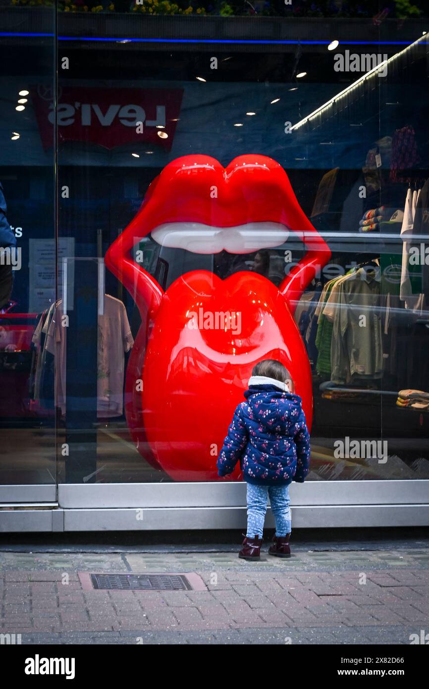 A small child stands in front of a shop window intrigued by  alarge red sculpture of lips. The Rolling Stones shop,  Carnaby Street, London, England, Stock Photo
