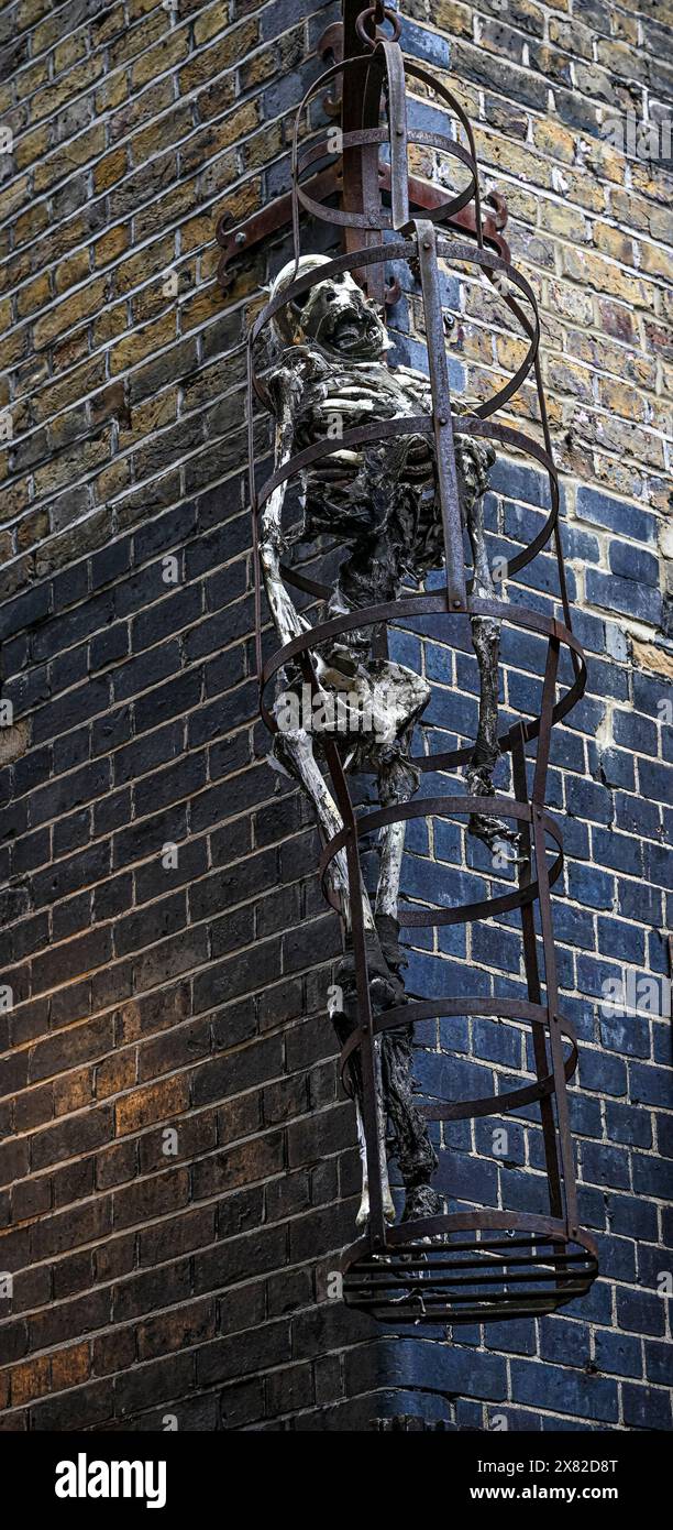 A rusted circular metal frame with a skeleton hangs against a brick wall. The Clink Prison Museum, London, England. Stock Photo