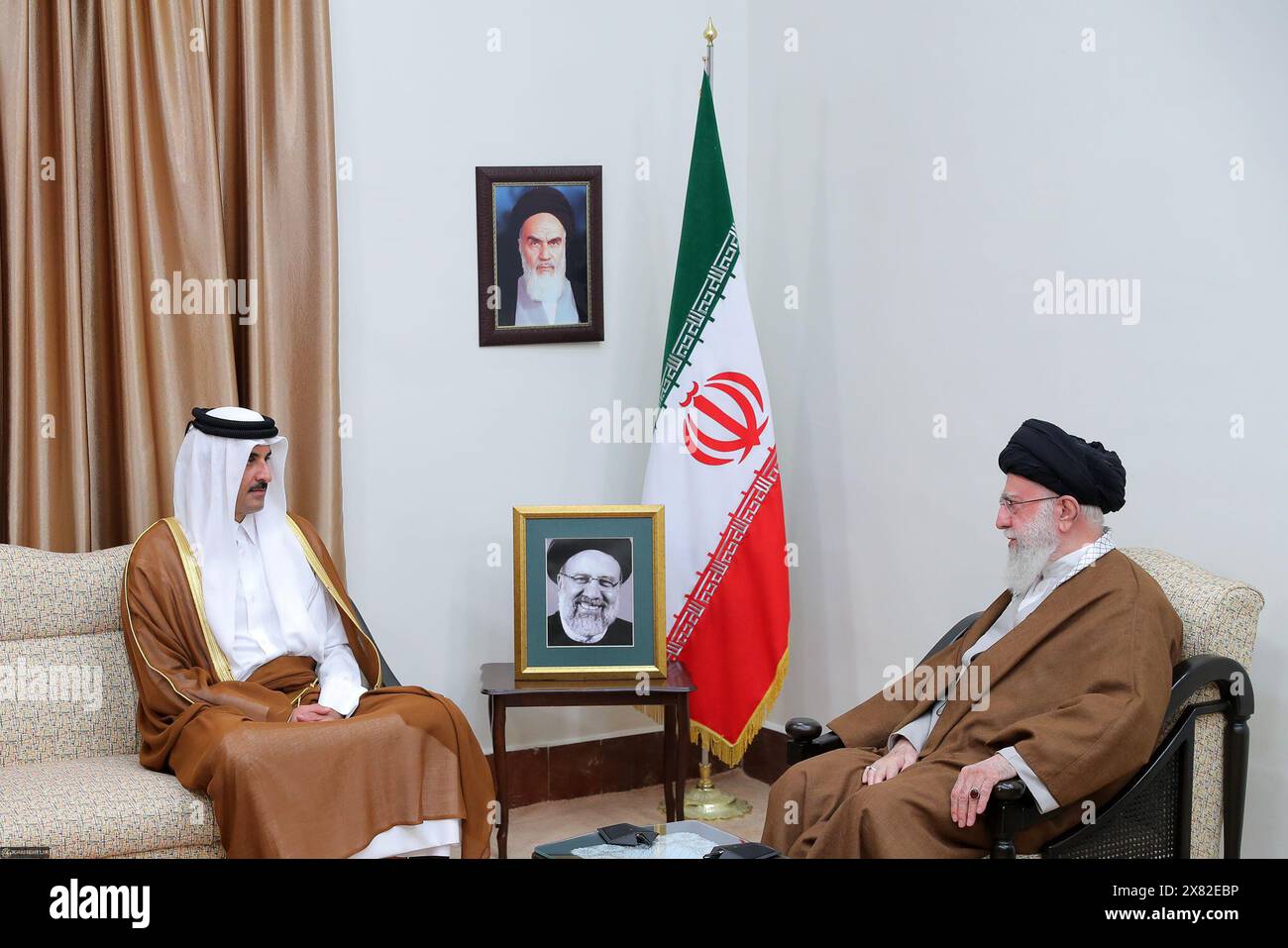 May 22, 2024, Tehran, Iran: Iranian Supreme Leader Ayatollah ALI KHAMENEI (R) is in talks with Qatar's Emir Sheikh TAMIM BIN HAMAD AL-THANI (C) during a meeting after the funeral ceremony of late President Ebrahim Raisi in Tehran. Portraits of the late Iranian revolutionary founder Ayatollah Khomeini and the top and late President Ebrahim Raisi are seen. Khamenei led prayers for late president Ebrahim Raisi on May 22, as huge crowds thronged the capital, Tehran, for his funeral procession. Raisi and his entourage died in a helicopter crash on May 20. (Credit Image: © Iranian Supreme Leader'S O Stock Photo
