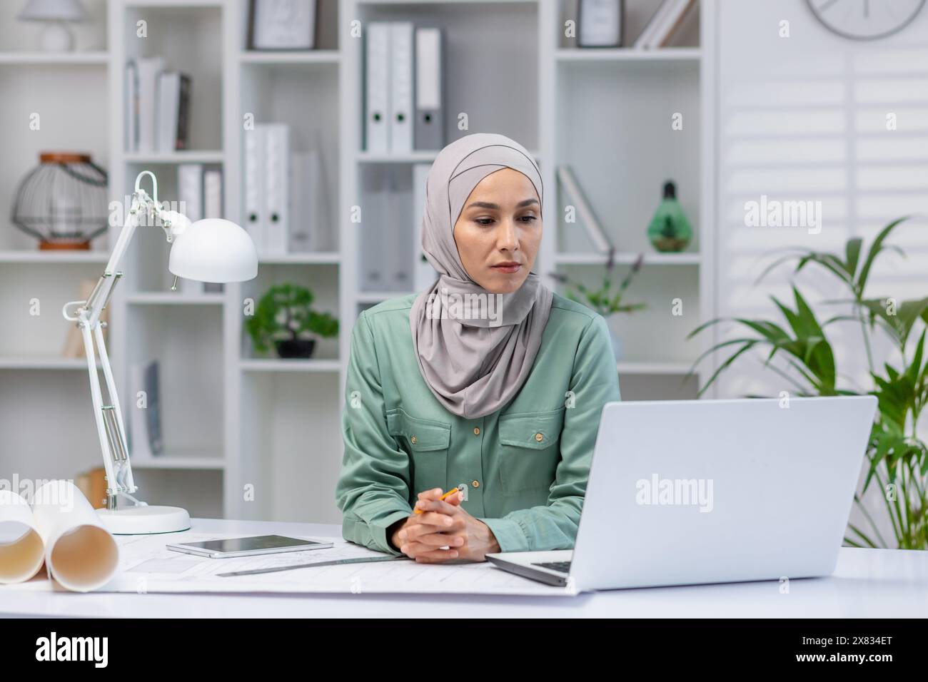 Woman in hijab designer working in home office, architect using laptop at work, studying technical assignment online, serious and concentrated reading. Stock Photo