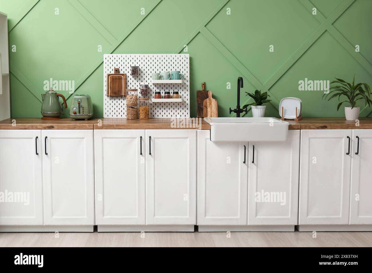 Interior of stylish kitchen with white counters, pegboard and green ...