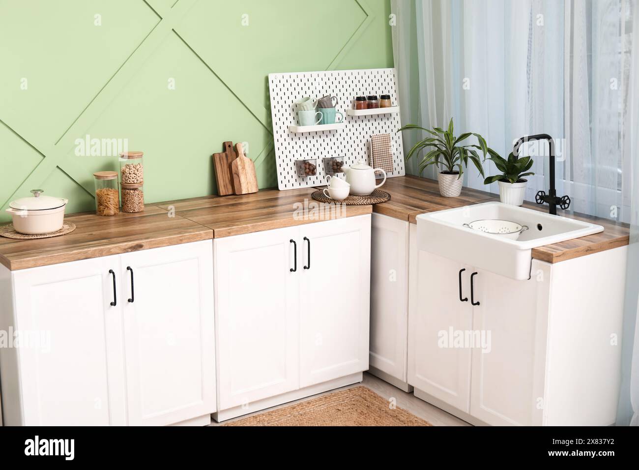 Interior of stylish kitchen with white counters, pegboard and green ...