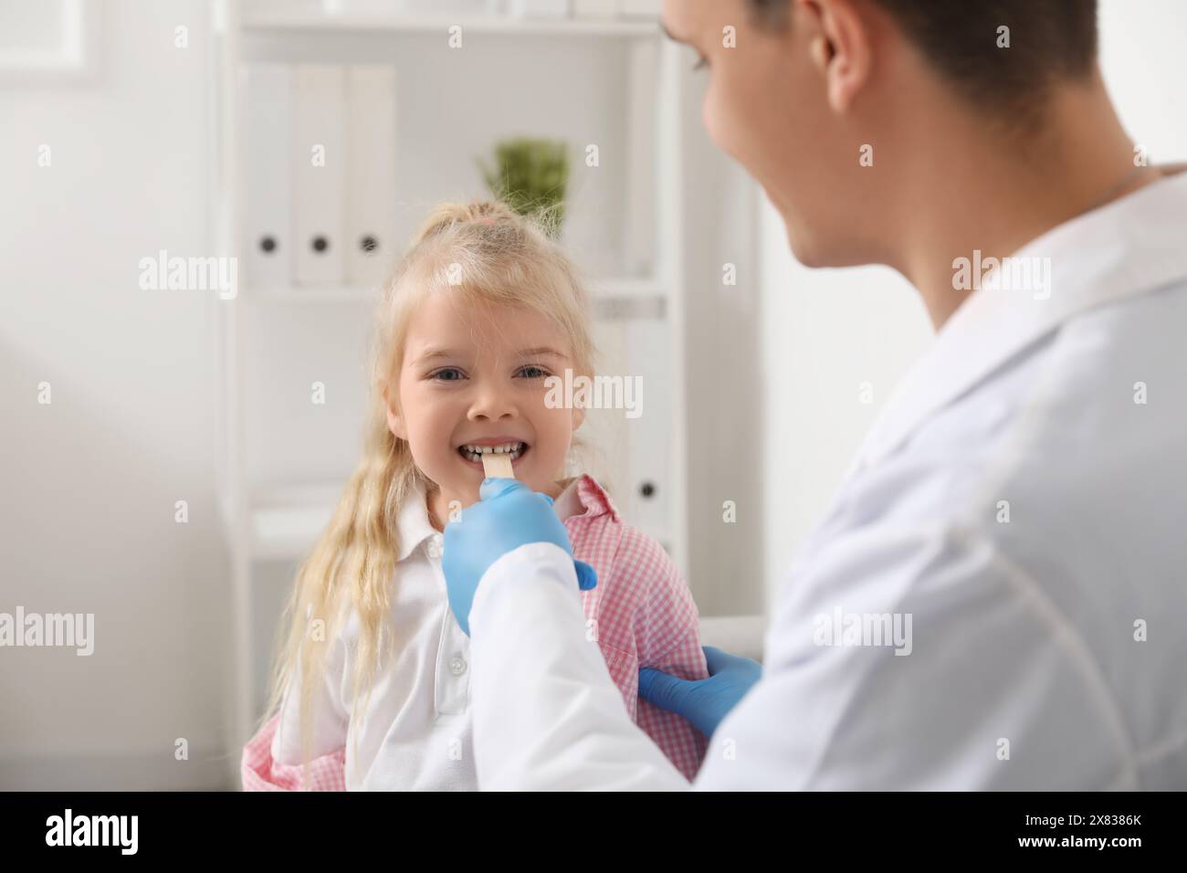 Male pediatrician examining little girl with tongue depressor in clinic