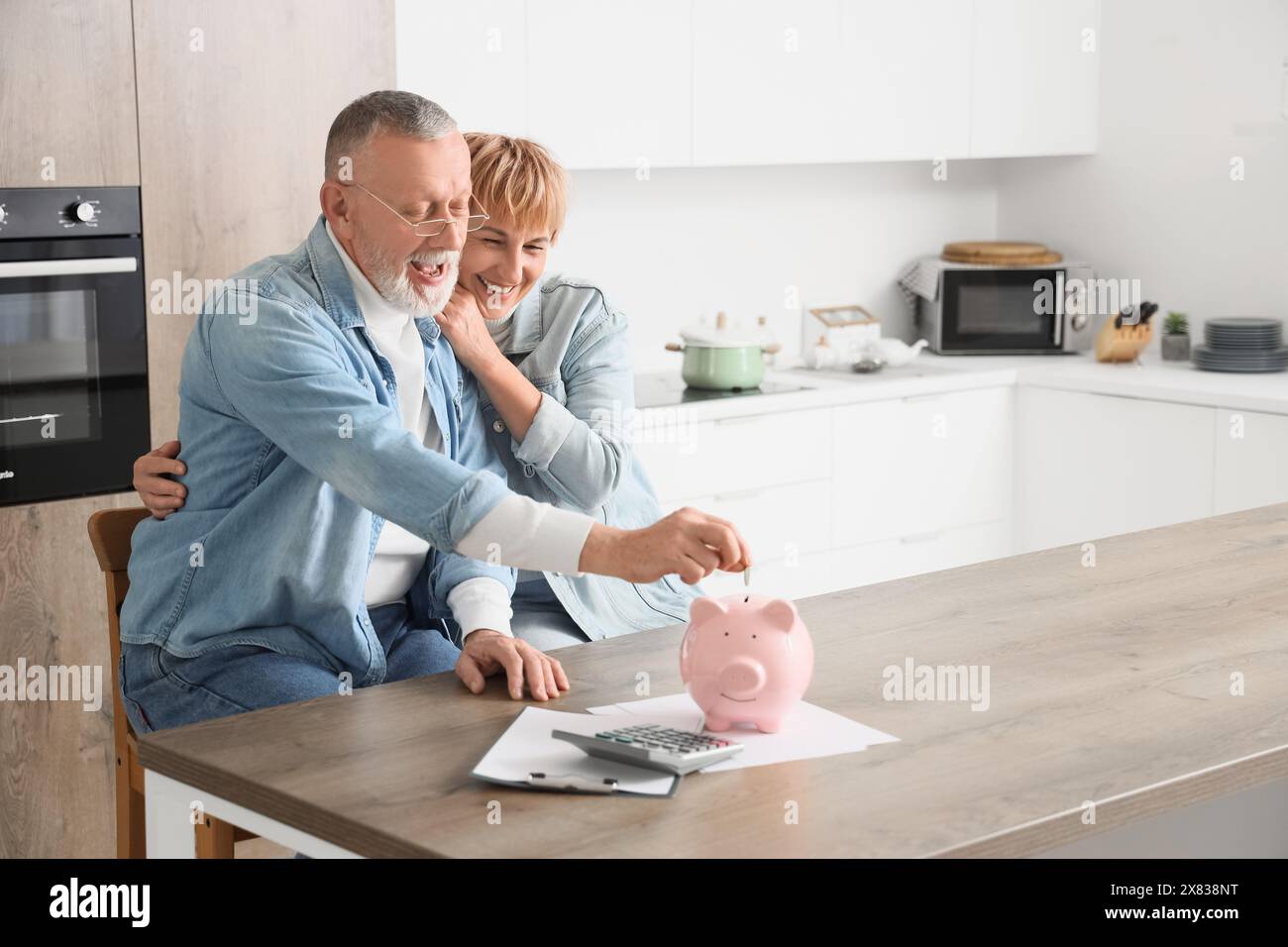 Mature couple putting coin into piggy bank in kitchen Stock Photo - Alamy