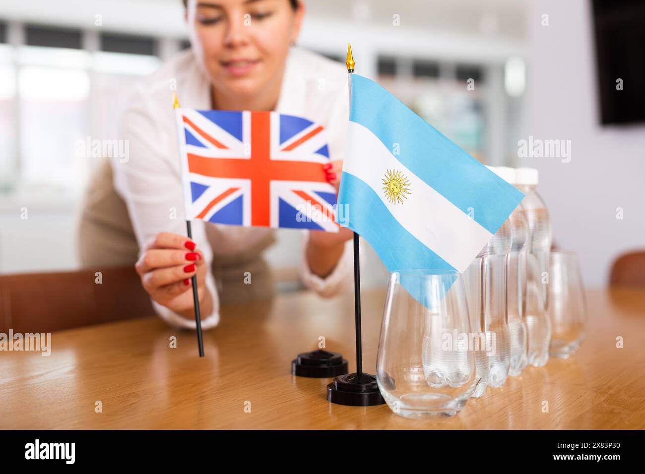 Little flag of Argentina on table and flag of Great Britain put next to it by young woman Stock Photo