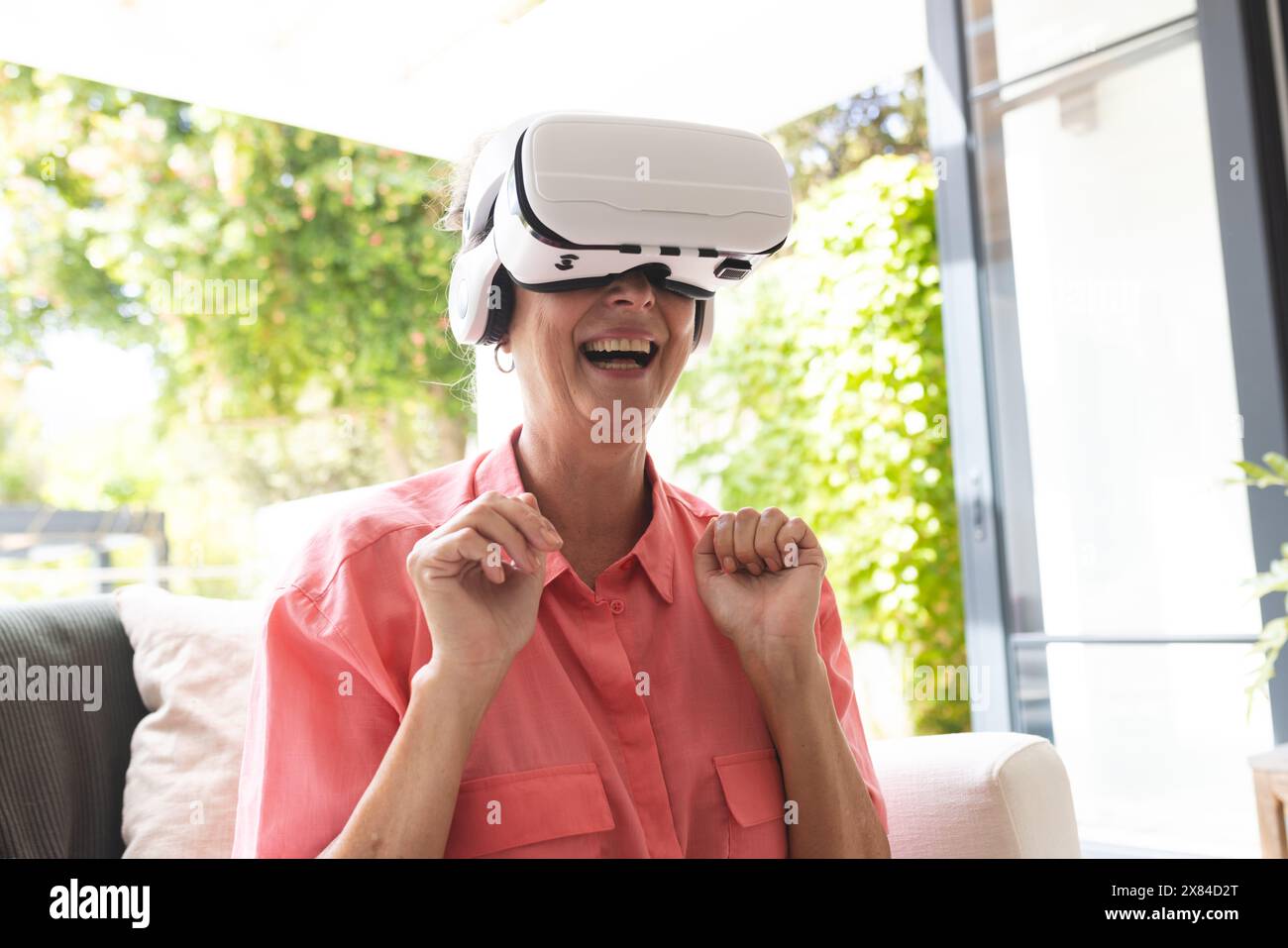 A Caucasian senior woman wearing virtual reality headset, laughing at home Stock Photo