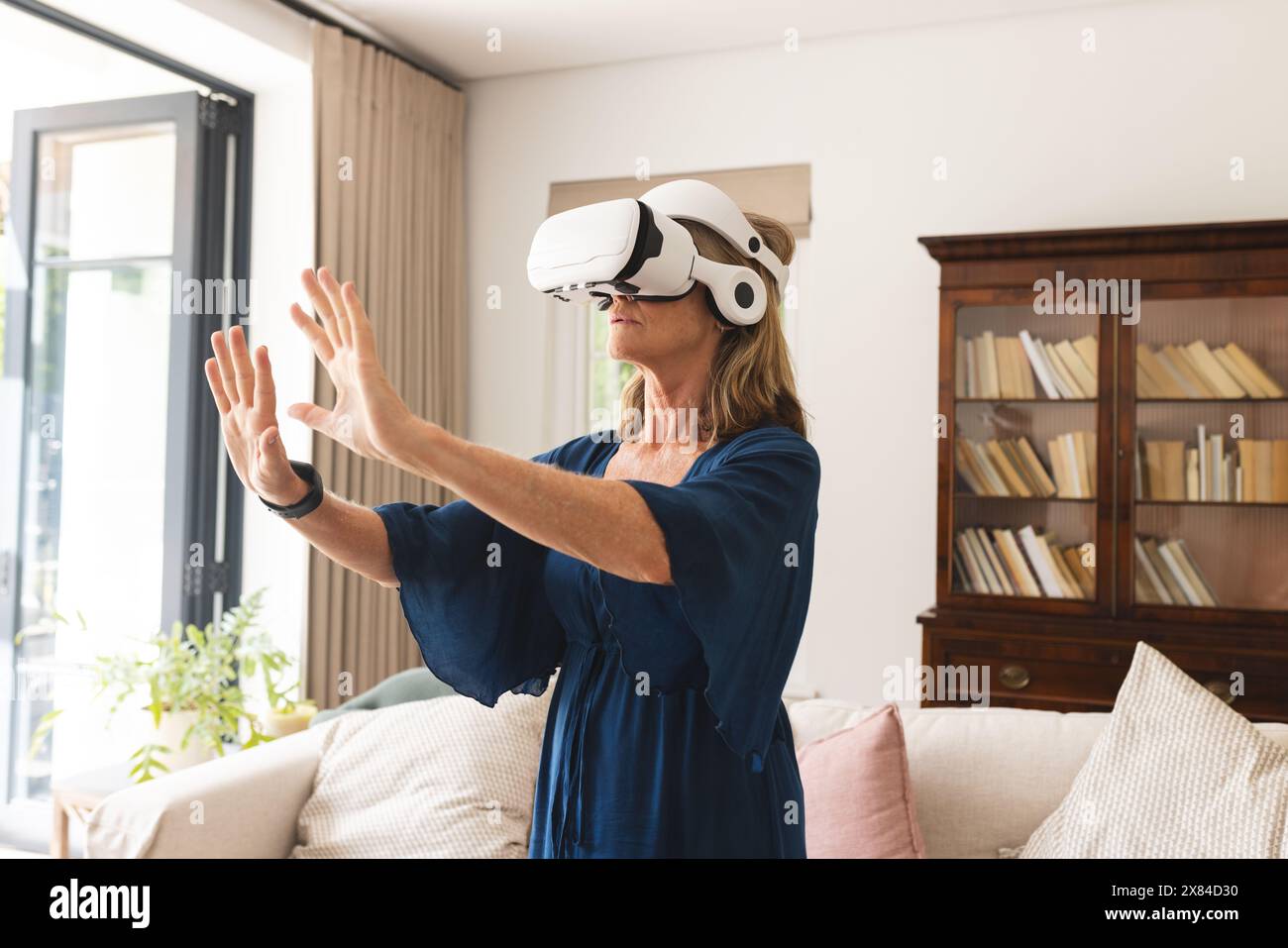 A senior Caucasian female wearing VR headset at home, standing in a living room Stock Photo