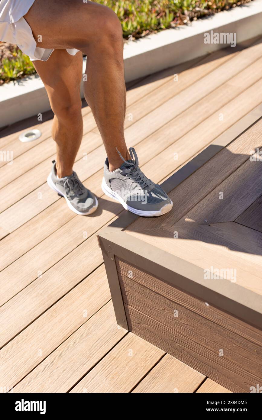 A biracial young male wearing running shoes stepping up on wooden bench outdoors Stock Photo