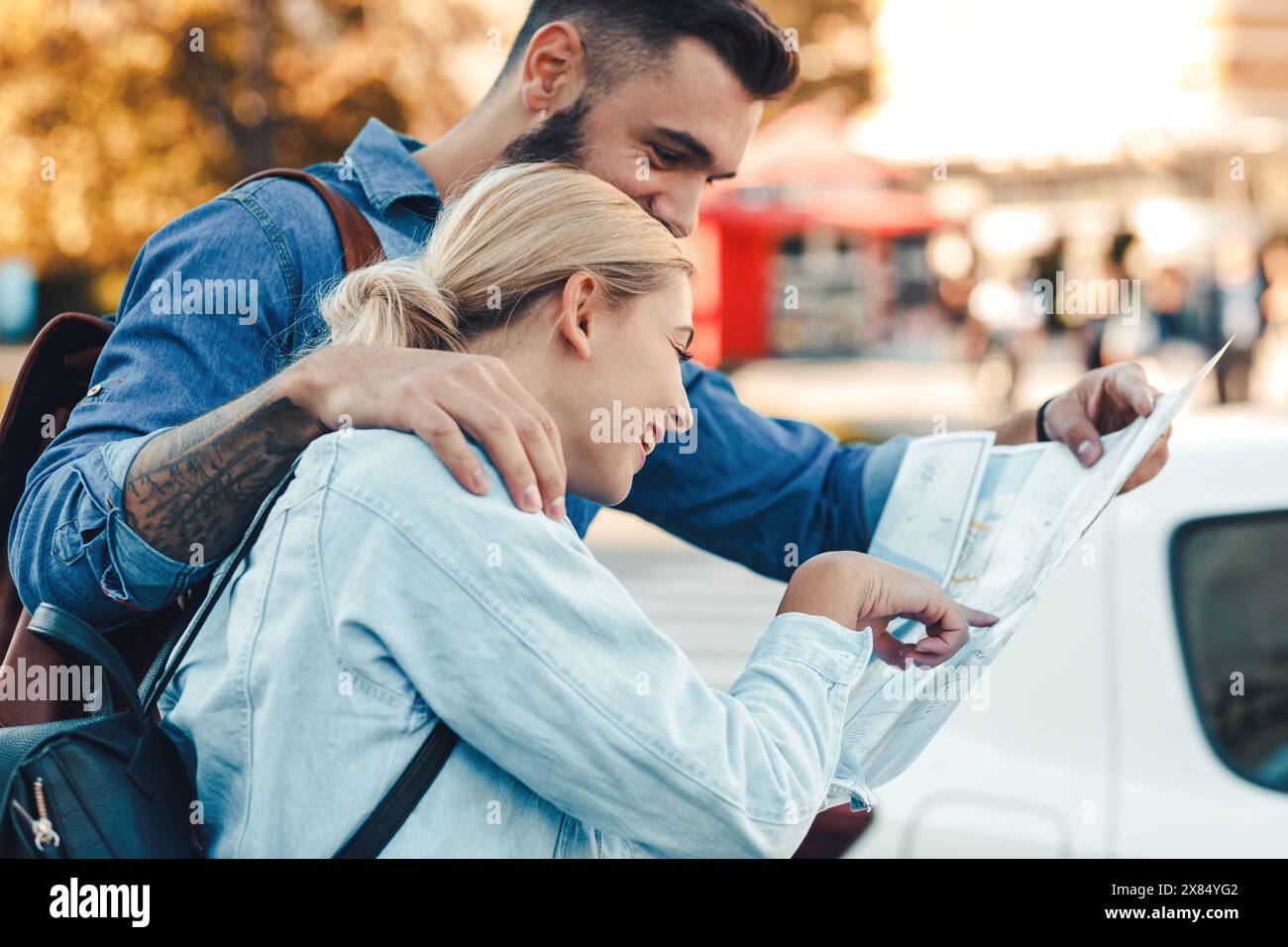 Smiling couple enjoying on vacation, young tourist having fun walking on city street looking at map for direction during the day. Stock Photo