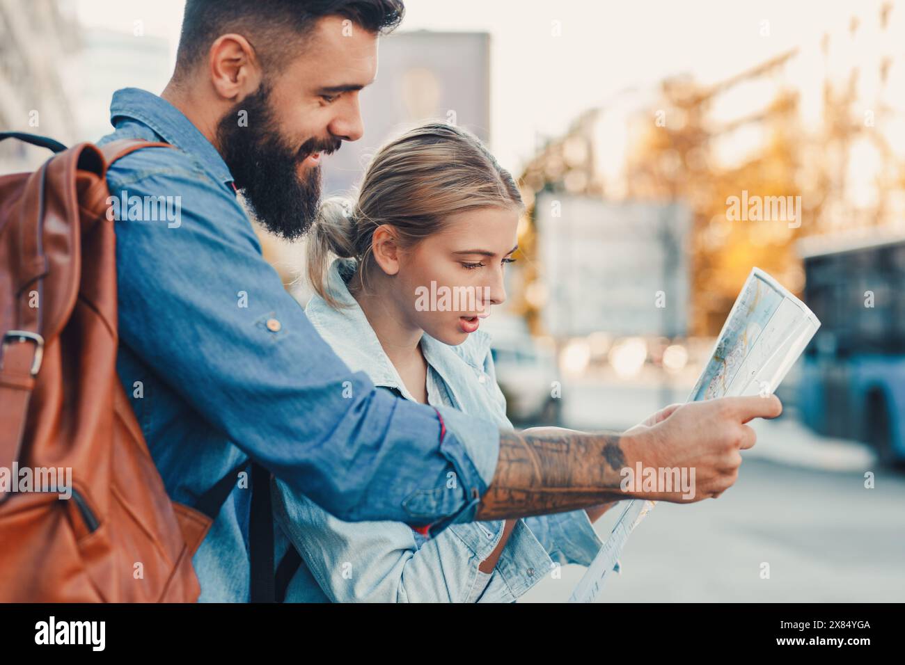 Smiling couple enjoying on vacation, young tourist having fun walking on city street looking at map for direction during the day. Stock Photo