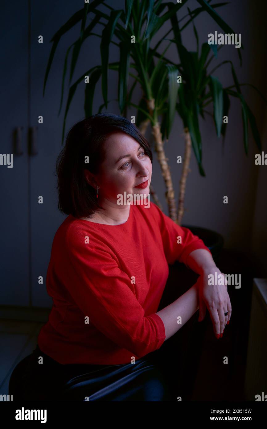 a portrait of a brunette with a bob haircut in a red sweater and a leather mini skirt in the office Stock Photo