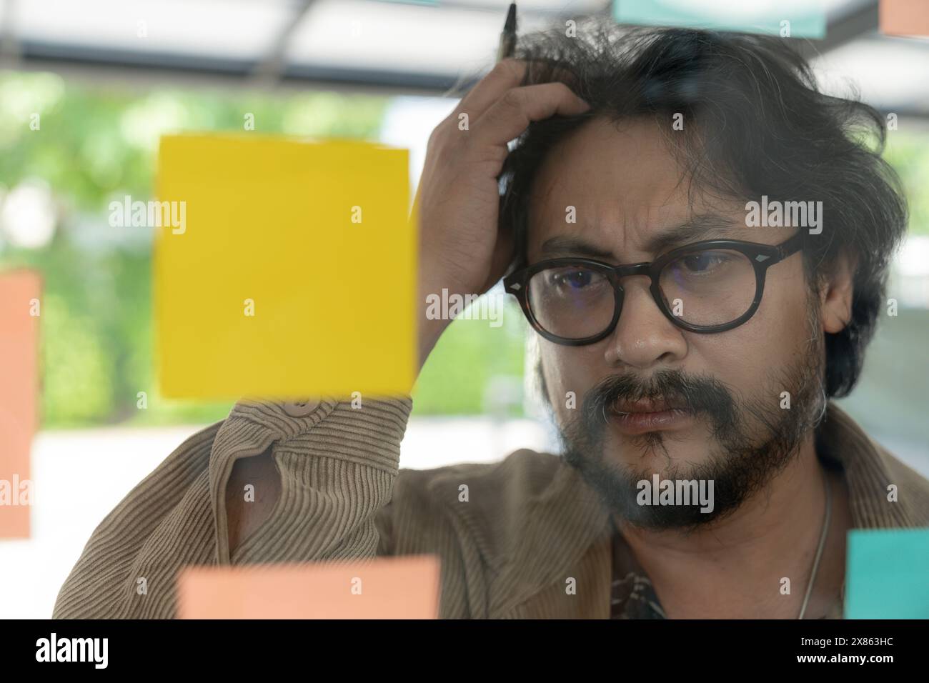 A man thinking and writing on sticky note on the wall. Stock Photo