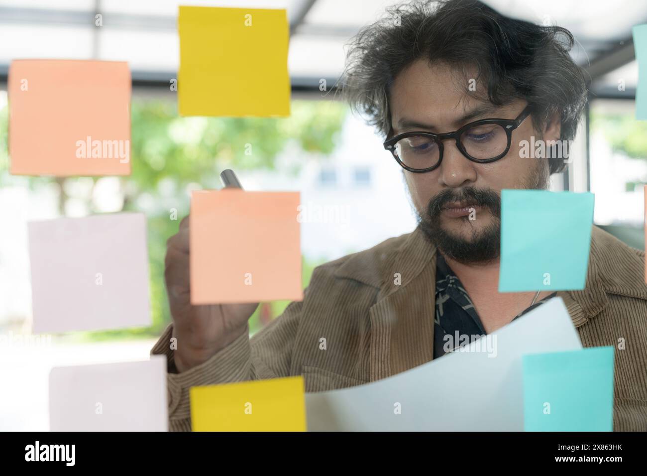 A man thinking and writing on sticky note on the wall. Stock Photo