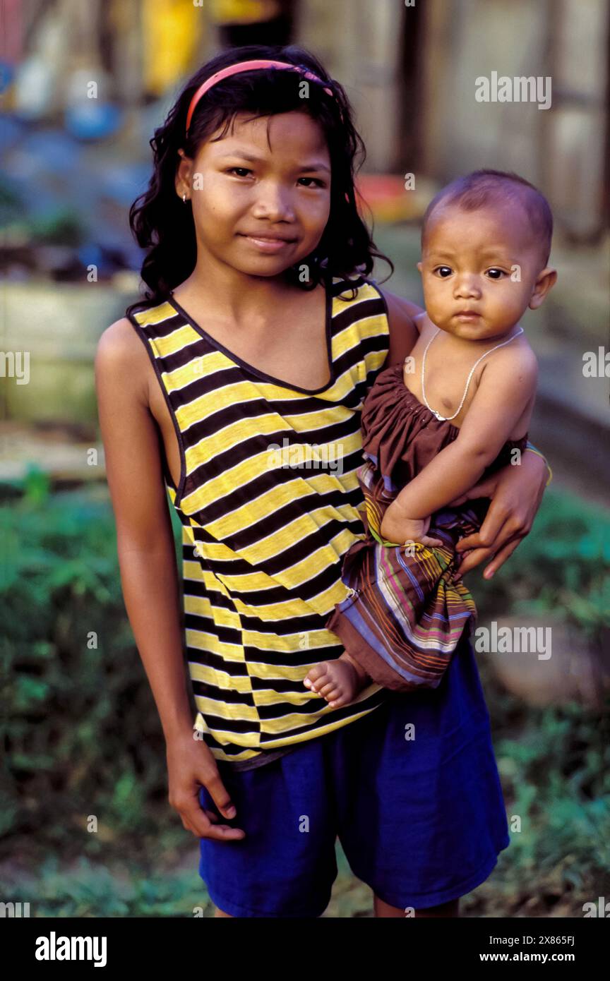 Philippines, Manila; girl carries her baby sister in a city slum.. Stock Photo