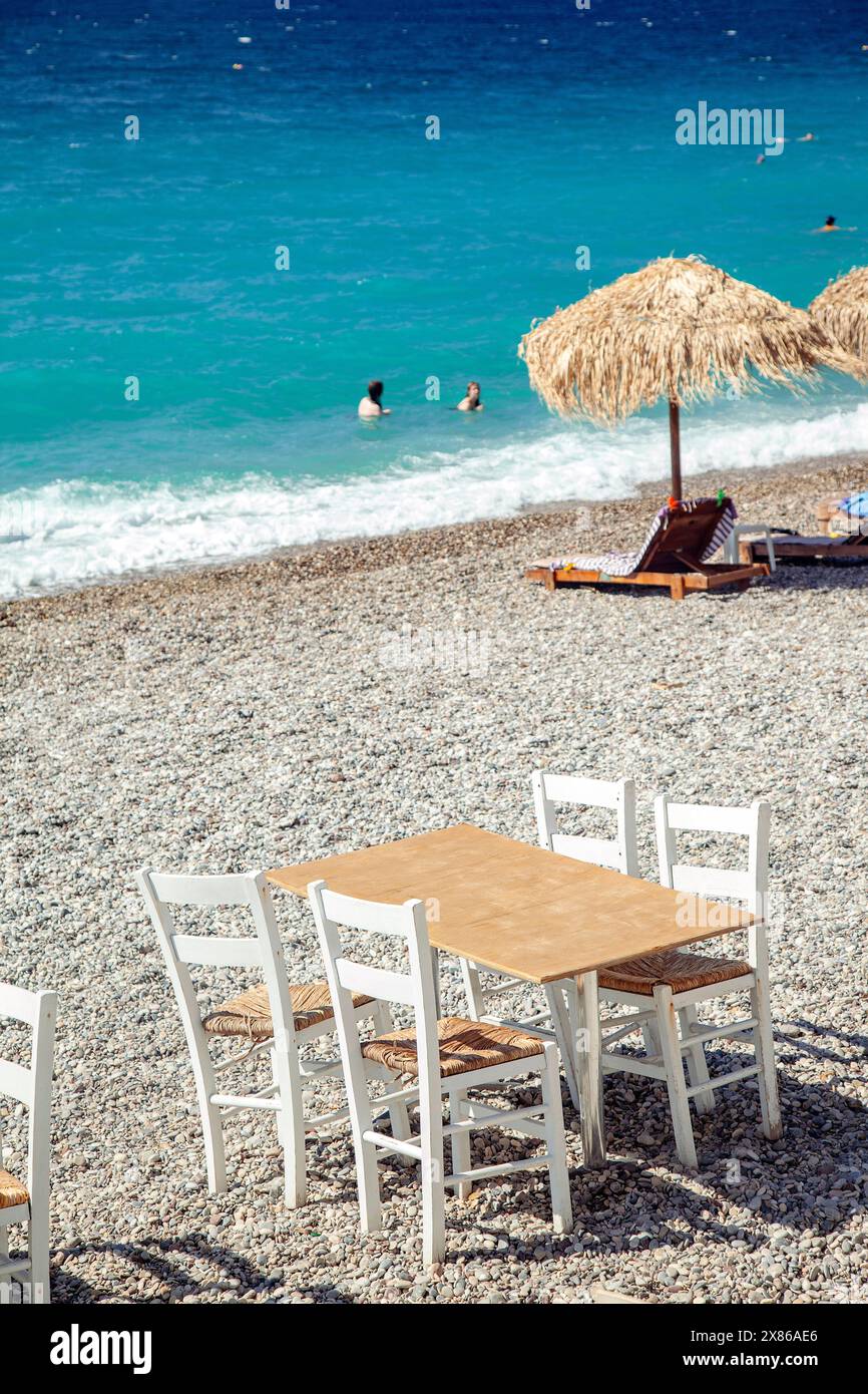 Wooden table with four wooden chairs, on the pebbled beach of Loutraki ...