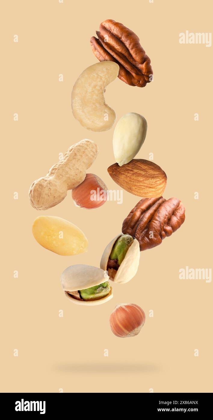 Many different nuts in air on beige background Stock Photo