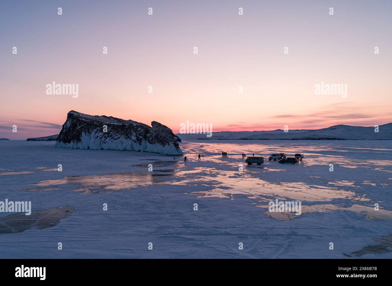 Aerial winter landscape of frozen lake Baikal. Groups of tourists got off the cars and walking around the rocky island in lake Baikal, walking on the Stock Photo
