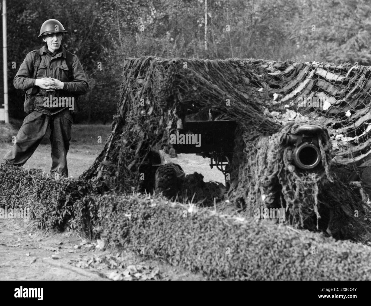 Ein Soldat der Englischen Streitkräfte steht neben einer getarnten Haubitze, Berlin 1961. - Originale Bildbeschreibung: 'Am Reichstag, Brandenburger Tor und der Straße des 17. Juni haben die britischen Besatzungstruppen Stellung bezogen' - Mit Panzern und getarnten Panzerraketengeschützen haben die britischen Einheiten Stellung bezogen, und zwar in den frühen Morgenstundendes heutigen Tages.' Stock Photo