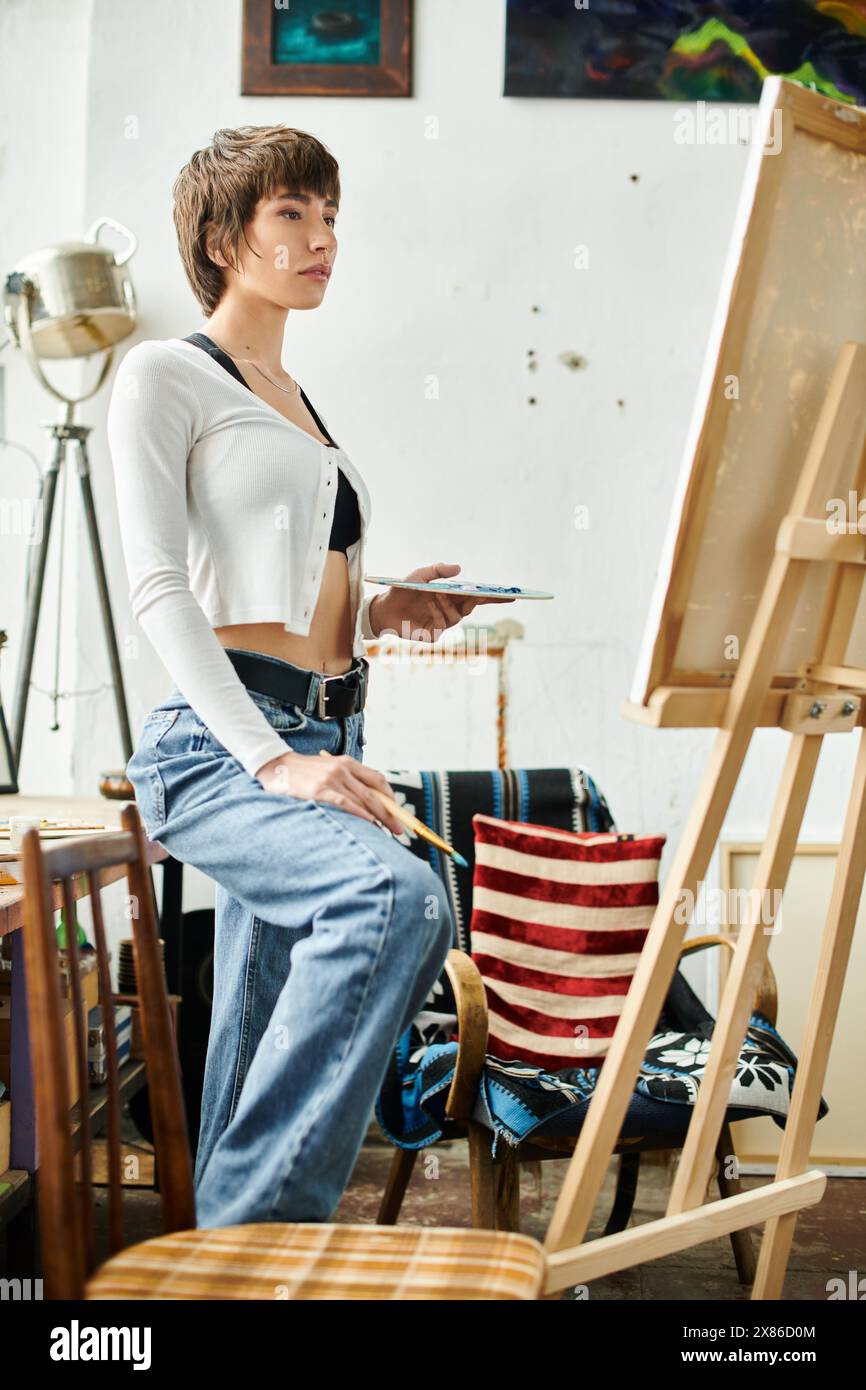 A woman seated in front of an easel, focusing on her artwork Stock ...