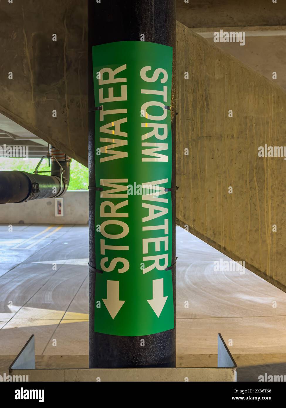 Closeup view of a metal pipe labeled storm water within a concrete parking garage, structure. Stock Photo
