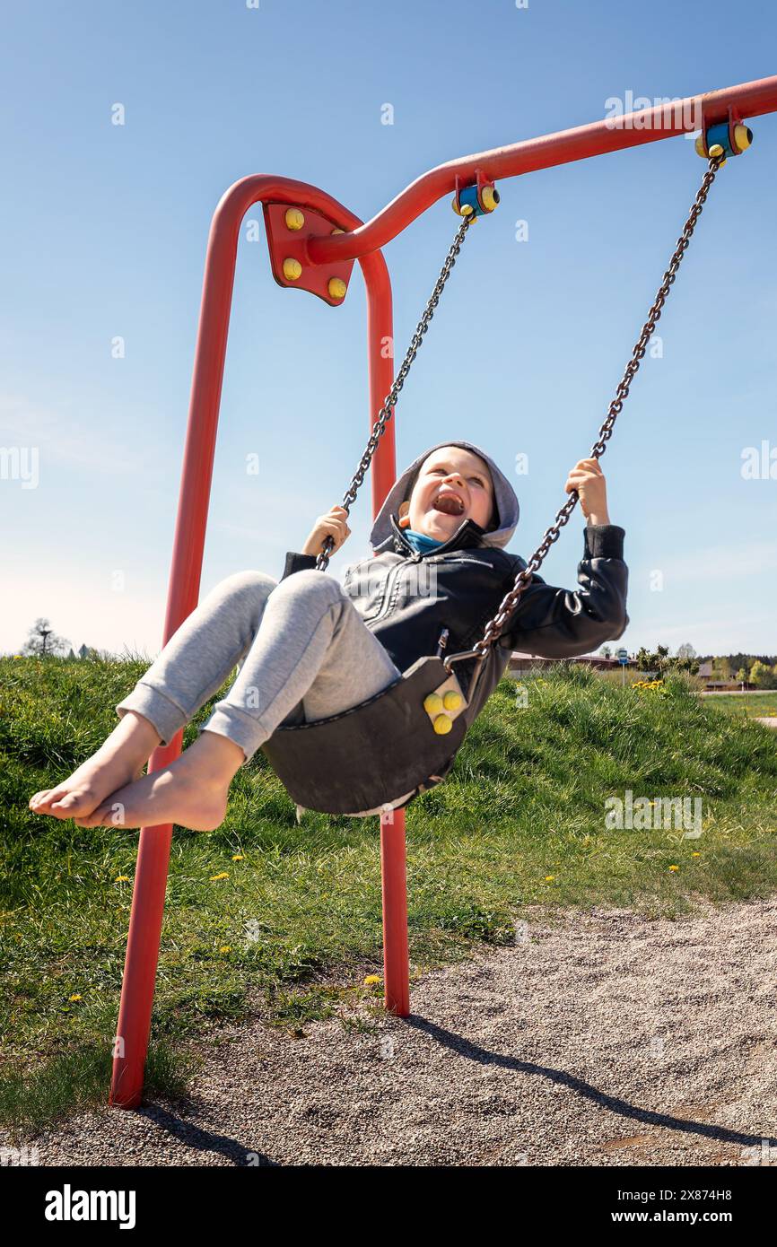 A strong emotion of childish joy, little boy swinging around on a chain swing outside. Stock Photo