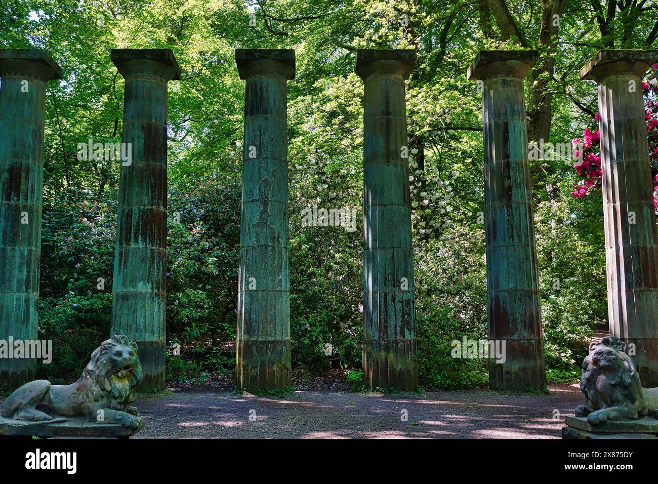 Ancient stone columns surrounded by lush greenery and two lion statues ...