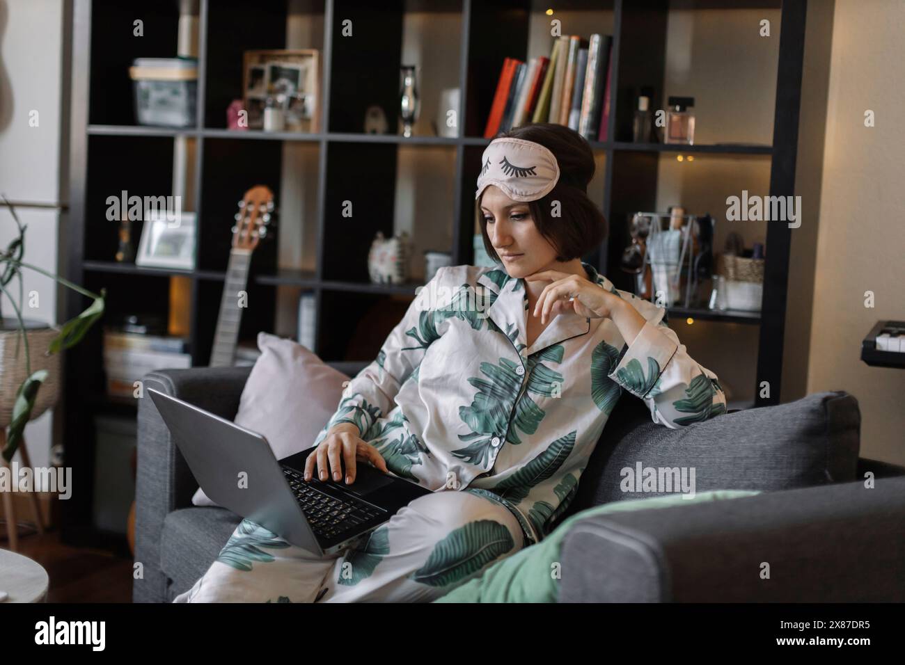 Young businesswoman in pajamas and eye mask using laptop working at home Stock Photo