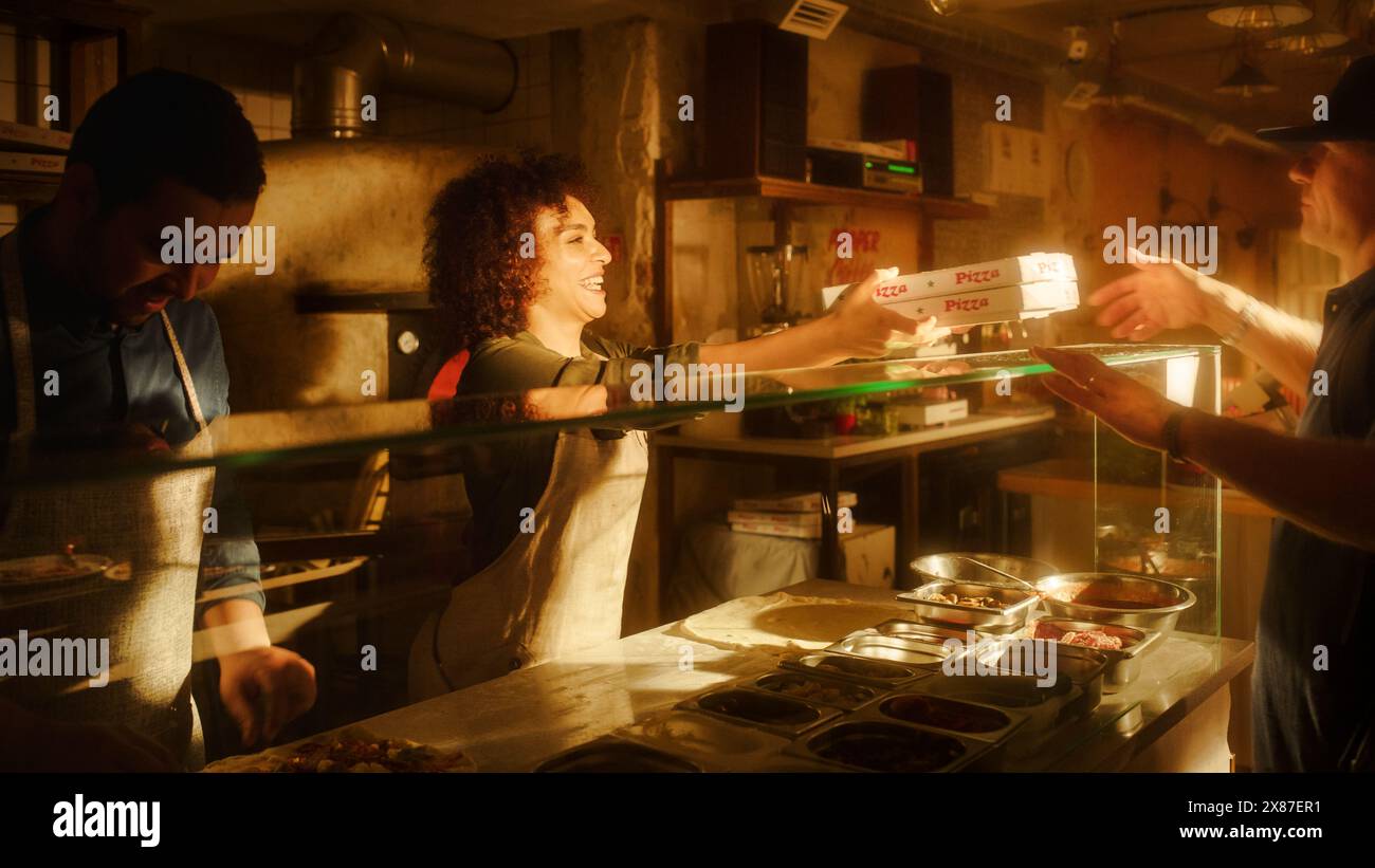 In Small Business Family Restaurant: Professional Couple of Chefs Preparing Pizza, Traditional Family Recipe, Giving Boxes to a Happy Customer. Authentic Sunny Pizzeria, Cooking Delicious Organic Food Stock Photo