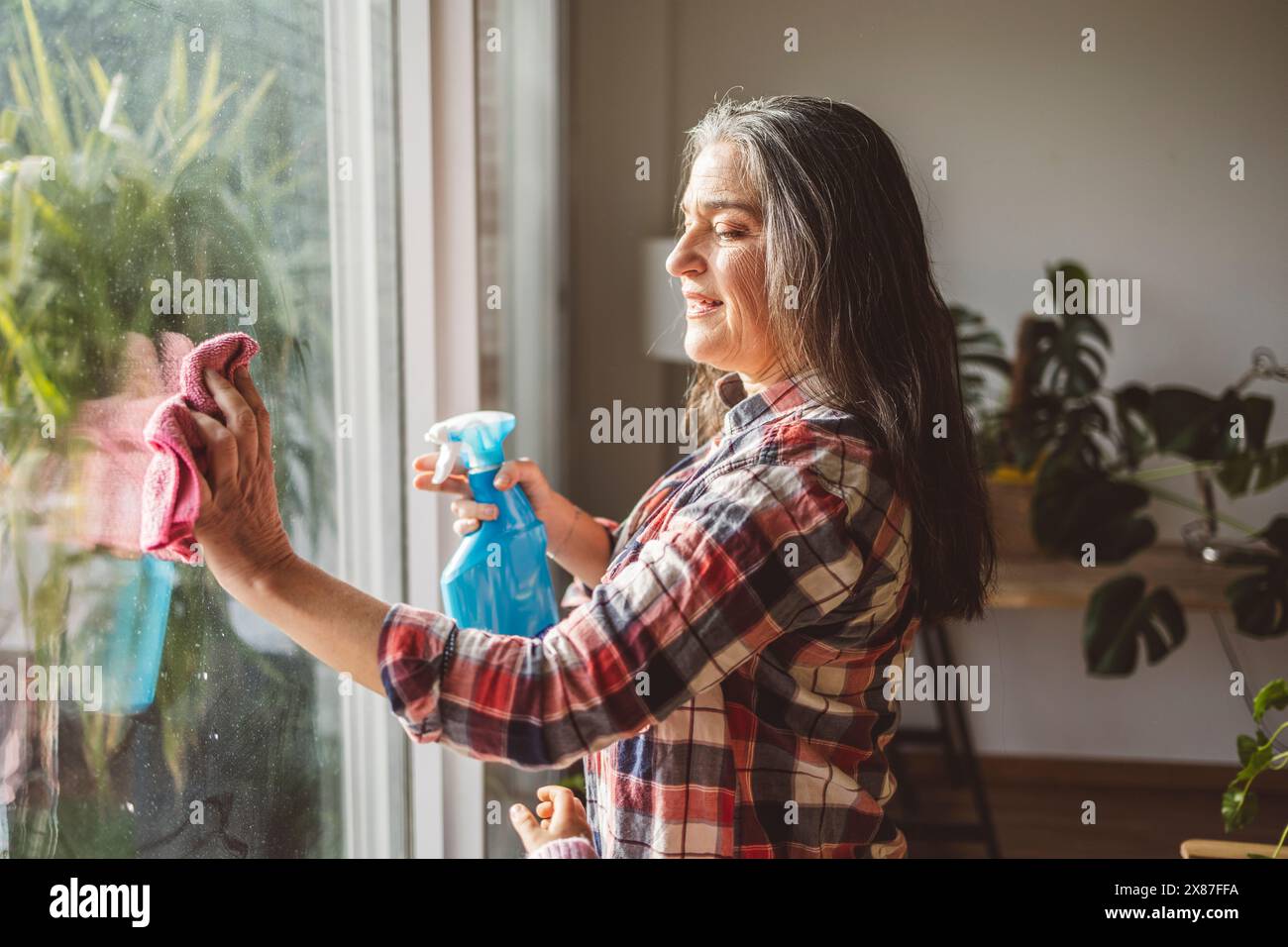 Mature woman cleaning window glass with rag at home Stock Photo - Alamy