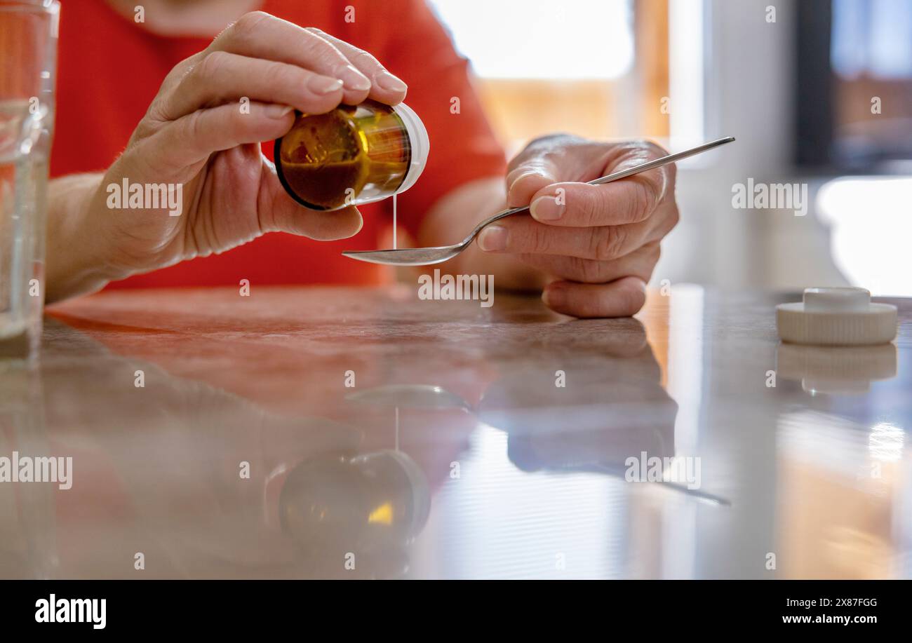 Woman pouring medicine in spoon from bottle at home Stock Photo
