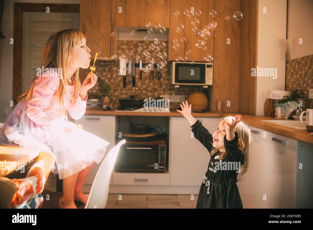 Siblings playing with soap bubble in kitchen at home Stock Photo