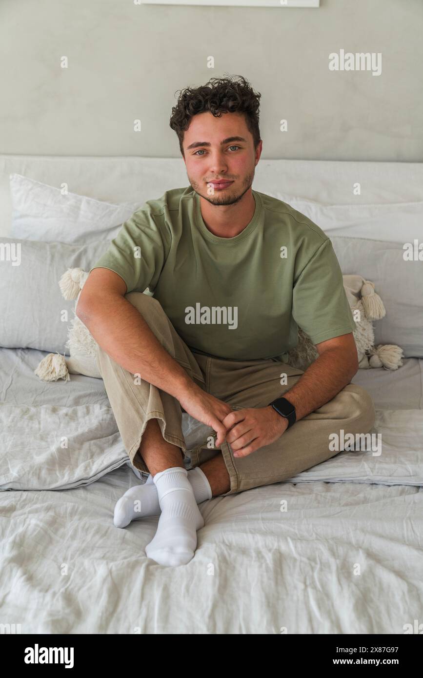 Smiling young man sitting on bed at home Stock Photo