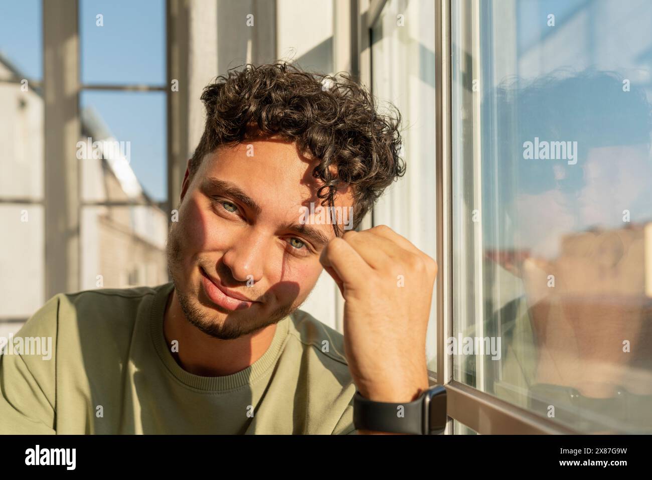 Smiling young man sitting near window Stock Photo