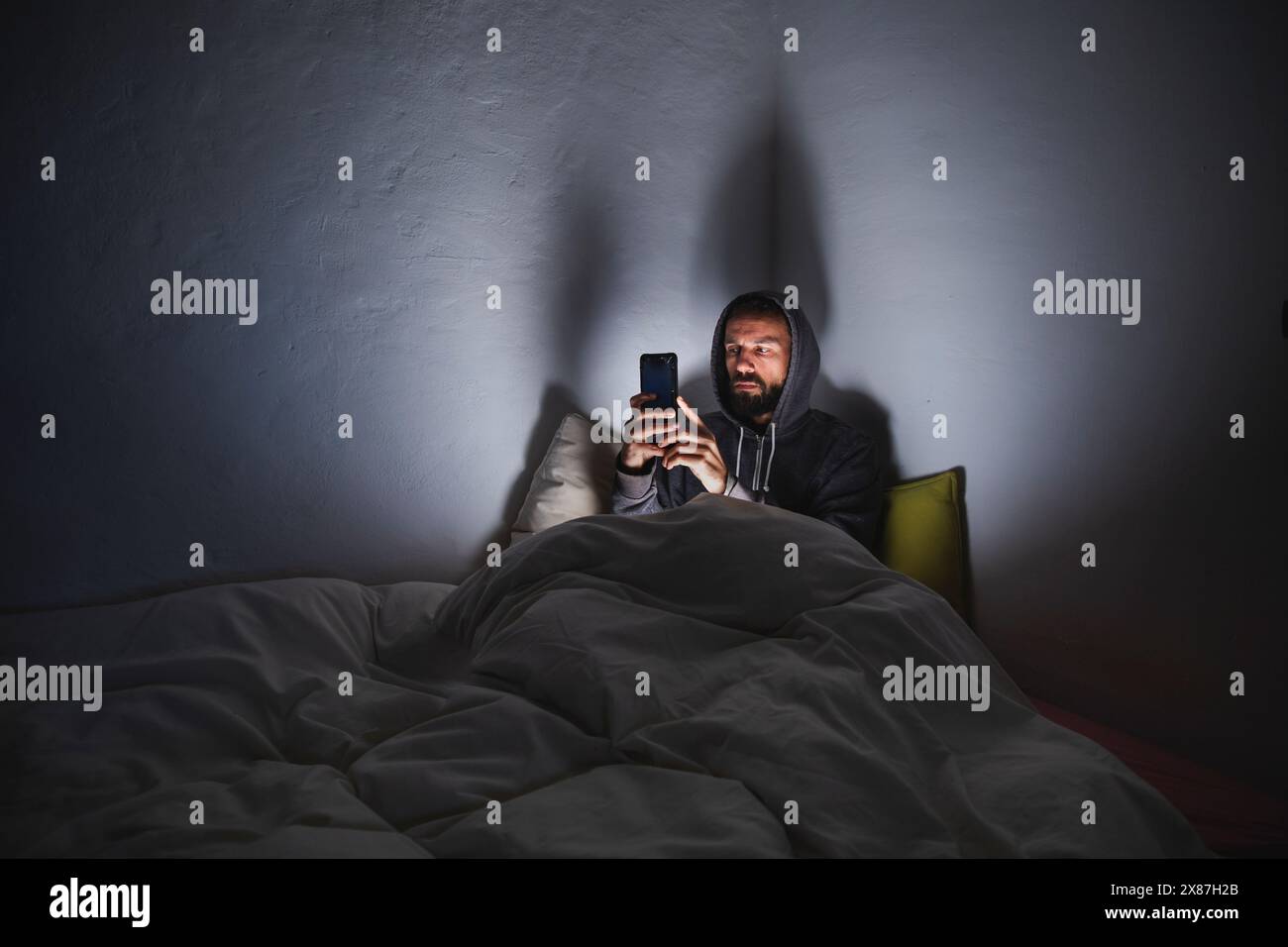 Man using smart phone sitting on bed in dark room Stock Photo