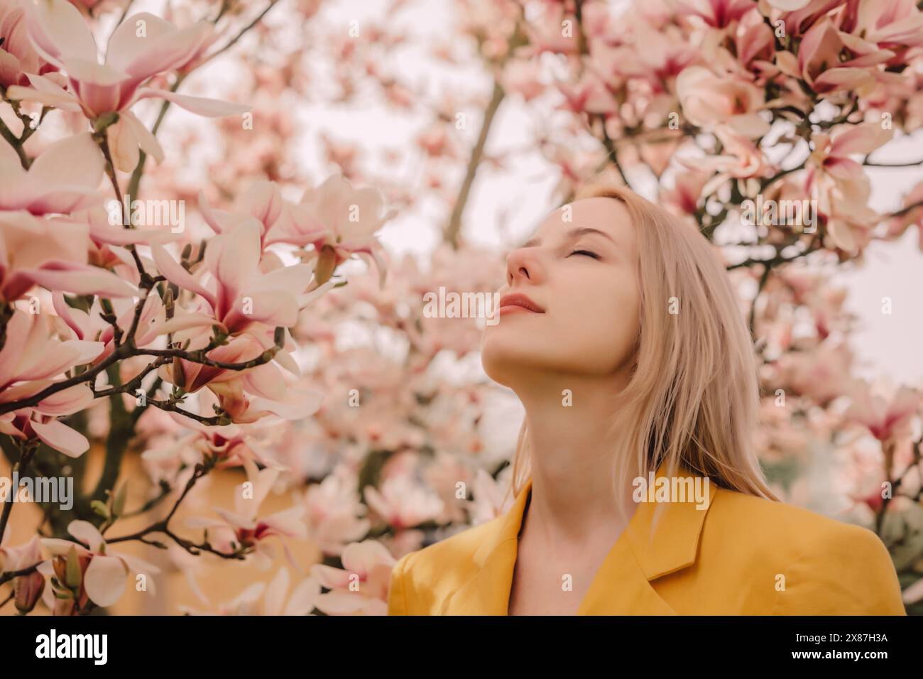 Blond woman with eyes closed by magnolia tree in garden Stock Photo - Alamy