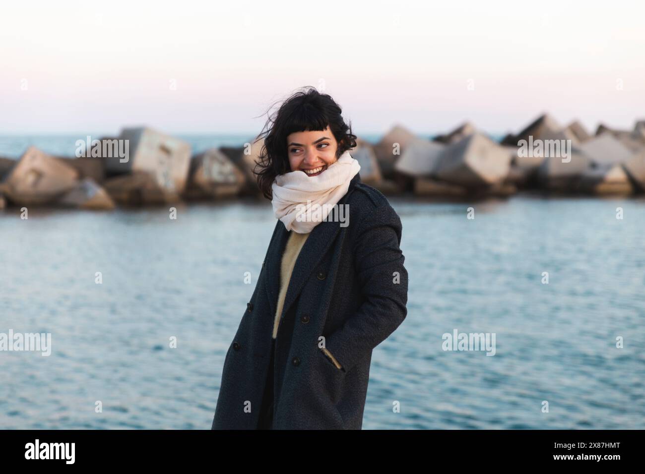 Happy woman in long coat standing near sea Stock Photo