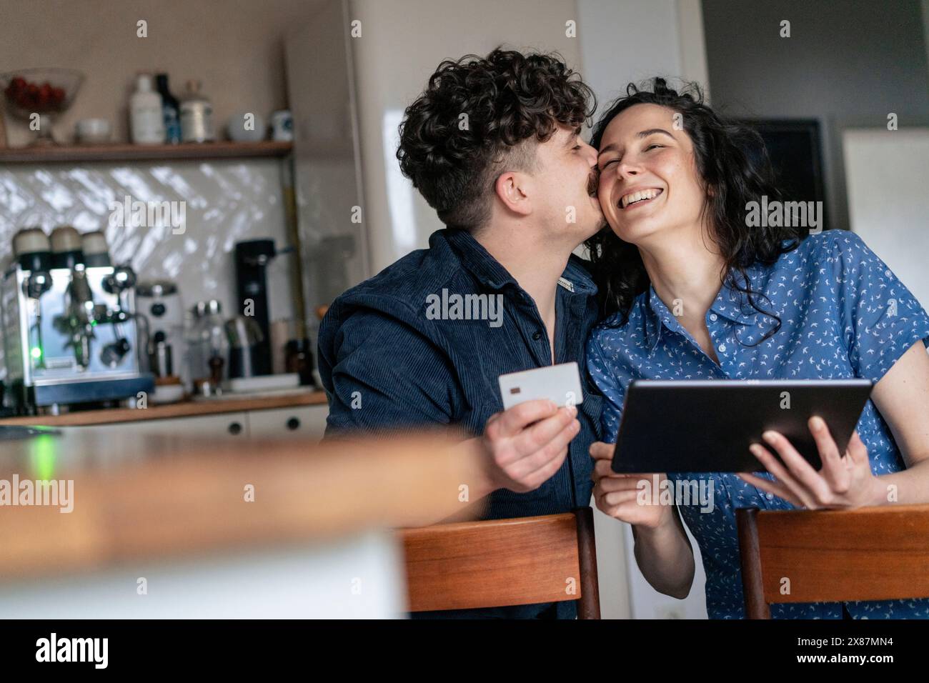 Man kissing girlfriend holding tablet PC in kitchen at home Stock Photo